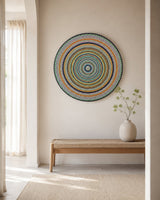 Golden Orange Orb original round mandala artwork displayed above a simple timber bench in a light neutral space